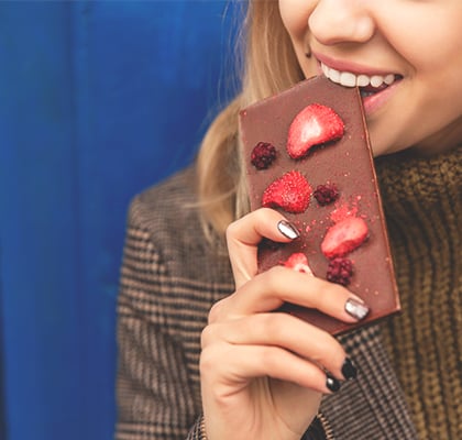 A woman bites on a chocolate bar to satisfy a craving for sweets. 