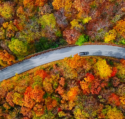 A car drives along a winding road during a road trip among the fall foliage. 