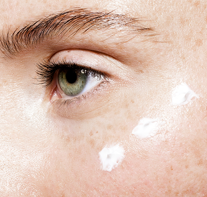 A woman applies eye cream the proper way as part of her skincare routine to reduce wrinkles and puffiness under the eyes.