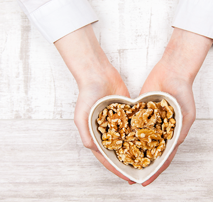A woman holds a bowl of walnuts to snack on for glowing skin as part of her self-care routine.
